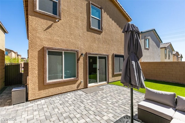 rear view of house featuring a patio, stucco siding, fence, and an outdoor living space