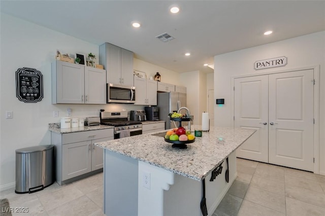 kitchen with appliances with stainless steel finishes, a center island with sink, light stone countertops, light tile patterned floors, and recessed lighting