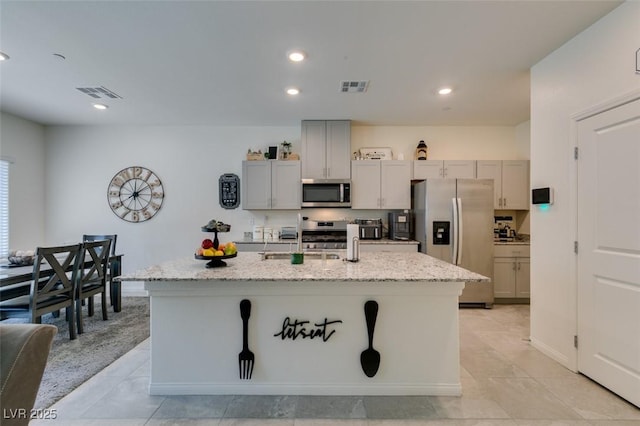 kitchen featuring appliances with stainless steel finishes, light stone countertops, an island with sink, recessed lighting, and a sink