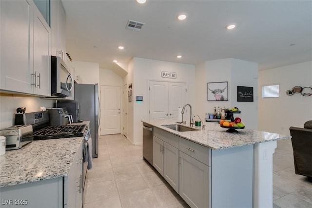 kitchen with stainless steel appliances, a sink, gray cabinetry, light tile patterned floors, and a kitchen island with sink