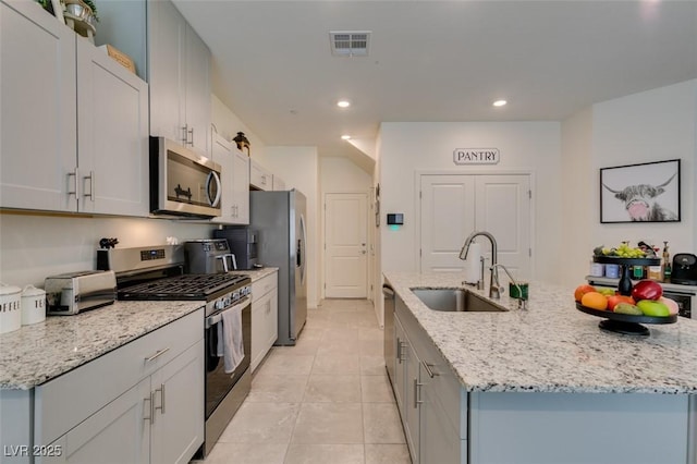 kitchen featuring stainless steel appliances, a sink, an island with sink, light tile patterned floors, and light stone counters