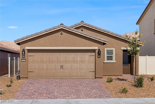 ranch-style house featuring fence, decorative driveway, a garage, and stucco siding