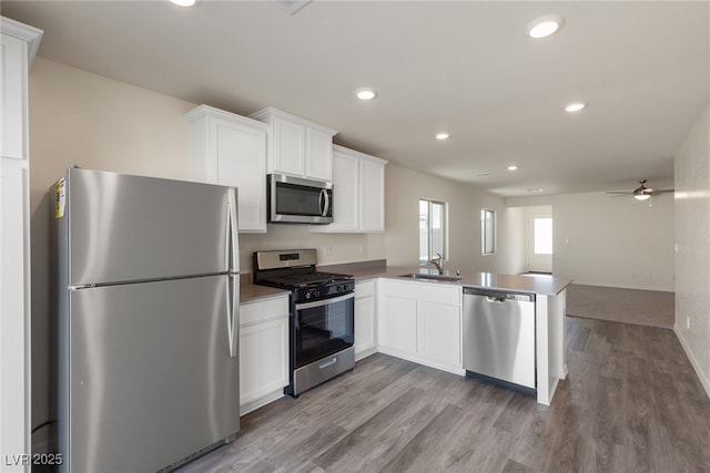 kitchen featuring appliances with stainless steel finishes, a peninsula, wood finished floors, a sink, and white cabinetry