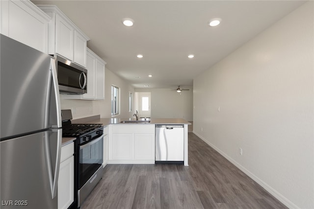 kitchen featuring stainless steel appliances, a sink, a peninsula, white cabinetry, and ceiling fan