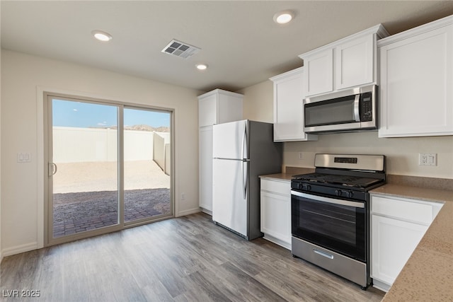 kitchen with appliances with stainless steel finishes, white cabinets, light wood-style flooring, recessed lighting, and baseboards
