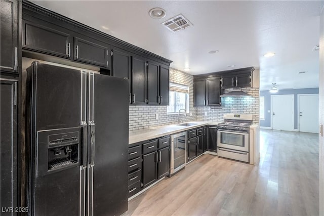 kitchen featuring gas stove, black fridge with ice dispenser, a sink, tasteful backsplash, and light countertops