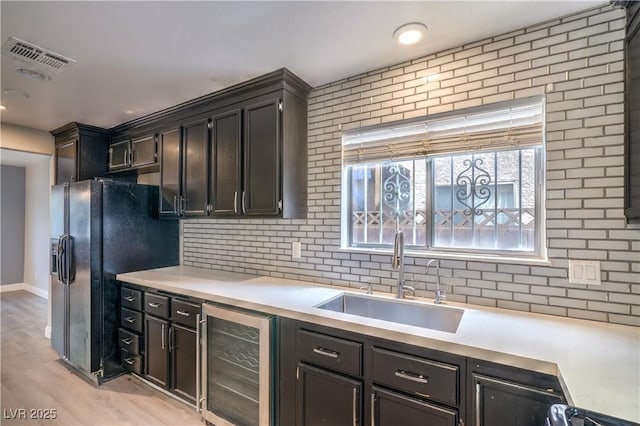 kitchen with beverage cooler, a sink, black refrigerator with ice dispenser, light countertops, and decorative backsplash
