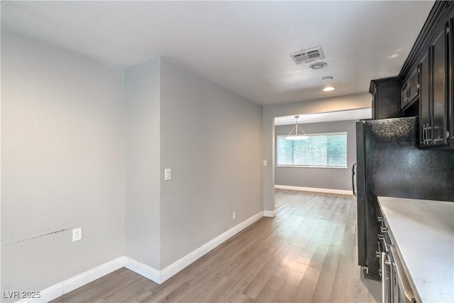 kitchen with light wood-style flooring, freestanding refrigerator, dark cabinetry, light countertops, and baseboards