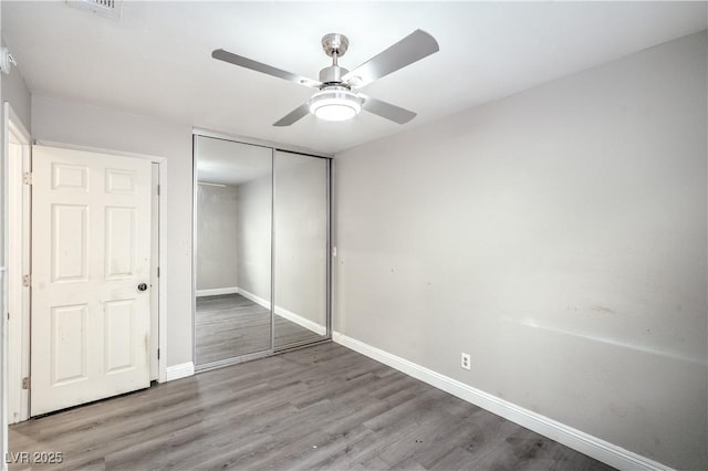 unfurnished bedroom featuring baseboards, wood finished floors, a closet, and ceiling fan