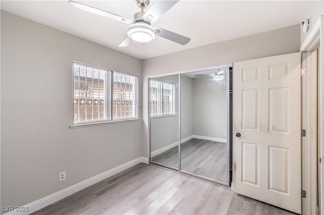 unfurnished bedroom featuring multiple windows, light wood-style floors, a closet, and baseboards