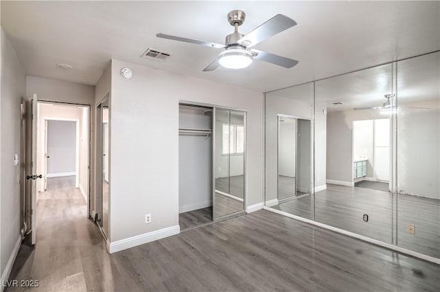 unfurnished bedroom with wood finished floors, baseboards, multiple closets, and a ceiling fan