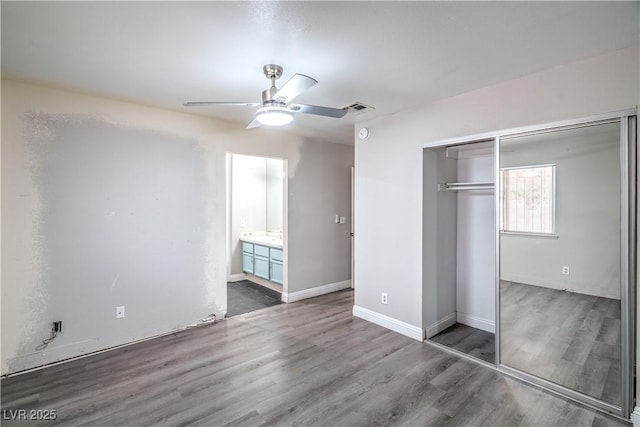 unfurnished bedroom featuring wood finished floors, a closet, ceiling fan, connected bathroom, and baseboards