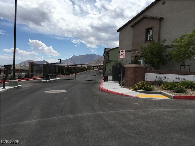 view of street with a gate, curbs, sidewalks, a mountain view, and a gated entry