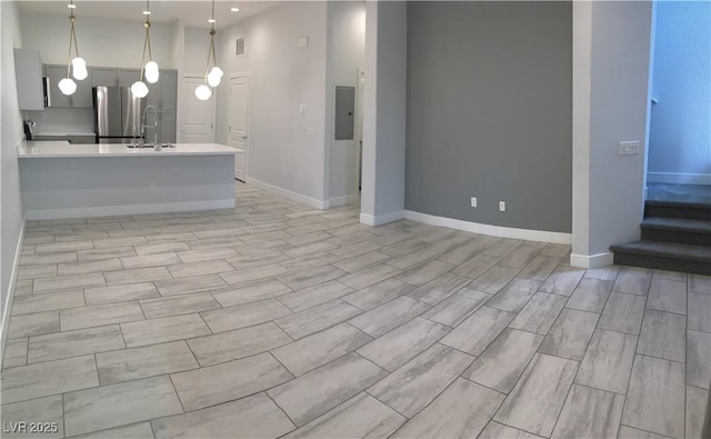 unfurnished living room with a sink, recessed lighting, electric panel, baseboards, and stairs
