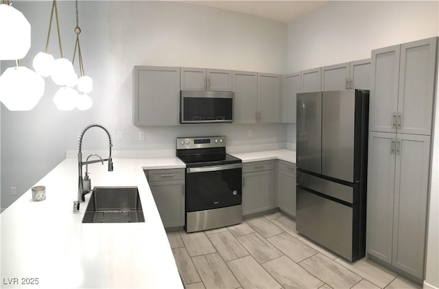kitchen featuring a sink, a peninsula, stainless steel appliances, gray cabinets, and light countertops