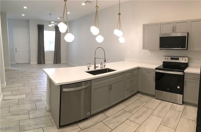 kitchen with a sink, a peninsula, gray cabinets, and appliances with stainless steel finishes