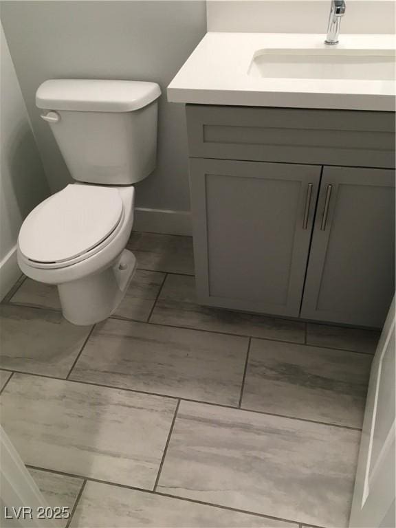 half bath featuring vanity, toilet, baseboards, and marble finish floor