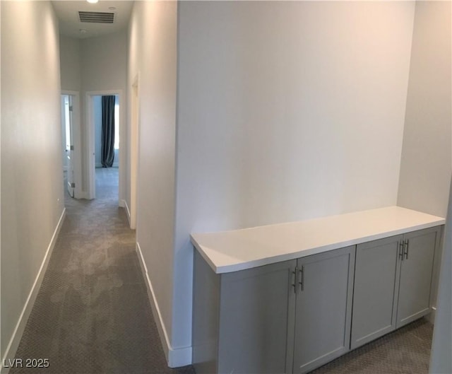 hall with dark colored carpet, baseboards, and visible vents