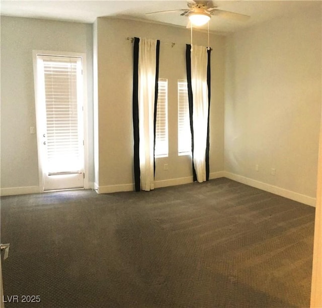 spare room featuring ceiling fan, dark colored carpet, and baseboards