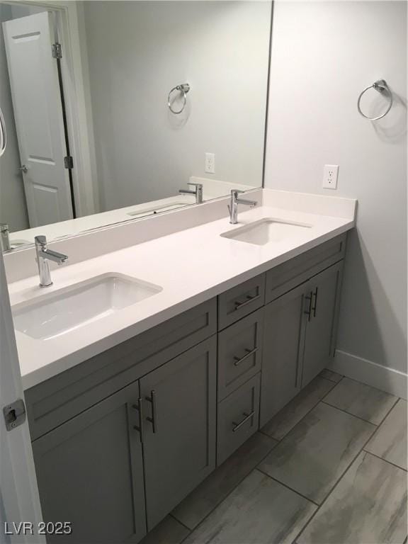 bathroom with double vanity, marble finish floor, baseboards, and a sink