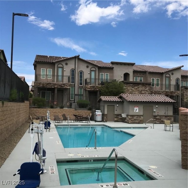 rear view of house with stucco siding, a hot tub, fence, and a community pool