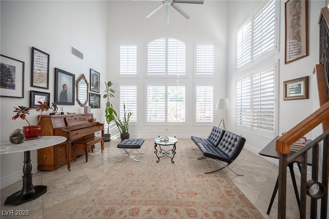 living area featuring a high ceiling, baseboards, and ceiling fan