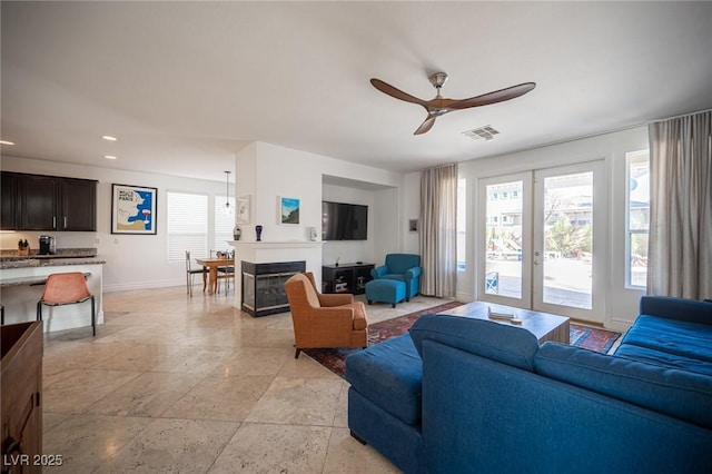 living area with ceiling fan, baseboards, stone tile flooring, a glass covered fireplace, and recessed lighting