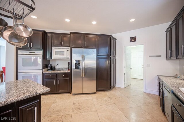kitchen featuring white appliances, dark brown cabinets, light stone counters, and recessed lighting
