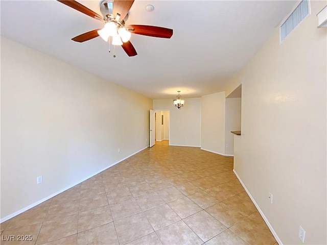 empty room with a chandelier, ceiling fan, light tile patterned flooring, and baseboards