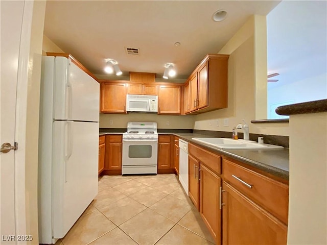 kitchen with white appliances, a sink, dark countertops, and light tile patterned flooring