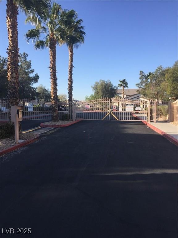 view of asphalt street with a gate, curbs, a gated entry, and sidewalks