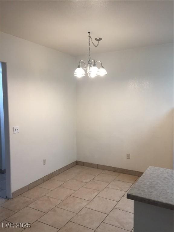 unfurnished dining area featuring a chandelier, light tile patterned floors, and baseboards
