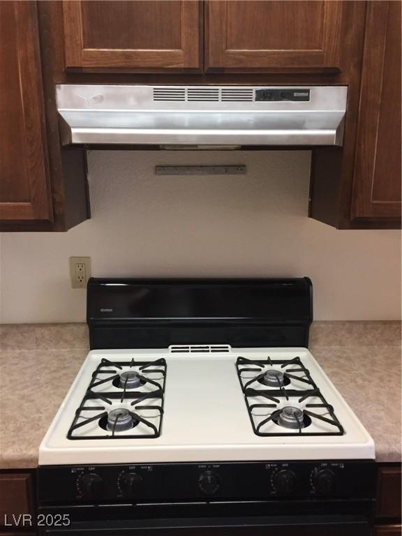 kitchen view of range with gas stovetop, under cabinet range hood, light countertops, and dark brown cabinetry