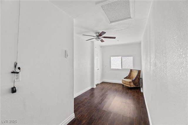 unfurnished room featuring dark wood-style flooring, baseboards, attic access, and a ceiling fan