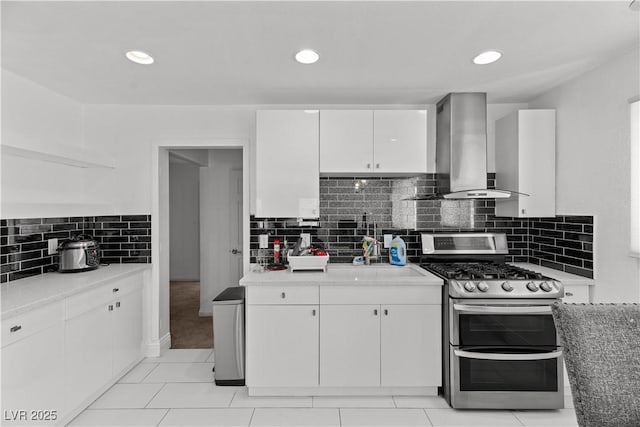 kitchen with double oven range, wall chimney exhaust hood, white cabinetry, light countertops, and recessed lighting