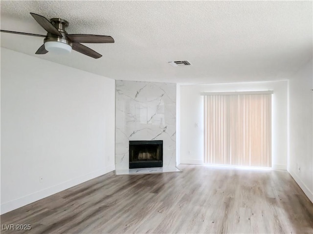 unfurnished living room with a textured ceiling, a fireplace, a ceiling fan, and wood finished floors