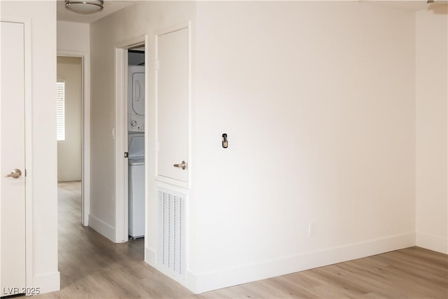 corridor with stacked washing machine and dryer, light wood-type flooring, and baseboards