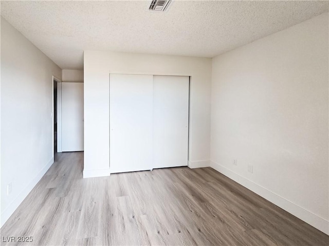 unfurnished bedroom with wood finished floors, a closet, baseboards, and a textured ceiling