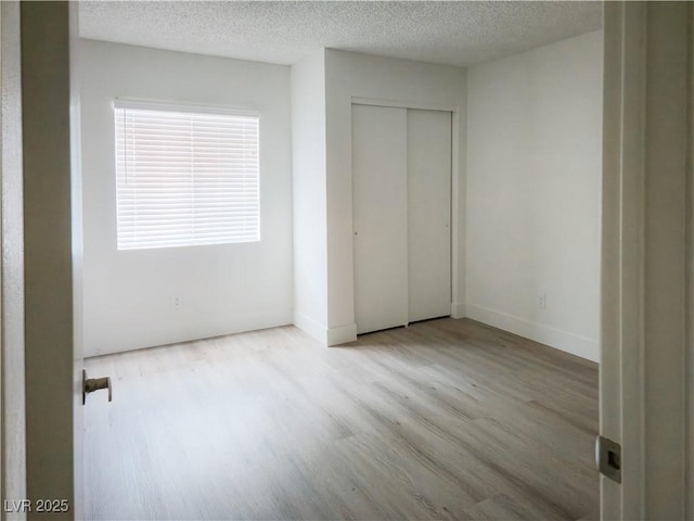 unfurnished bedroom with wood finished floors, a textured ceiling, a closet, and baseboards