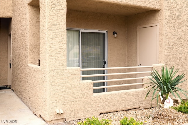 view of exterior entry featuring a balcony and stucco siding
