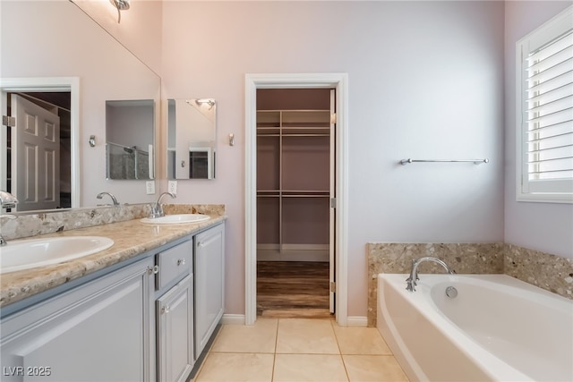 bathroom with a walk in closet, double vanity, tile patterned floors, a bath, and baseboards