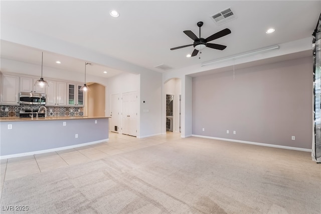 unfurnished living room with arched walkways, recessed lighting, ceiling fan, light colored carpet, and baseboards