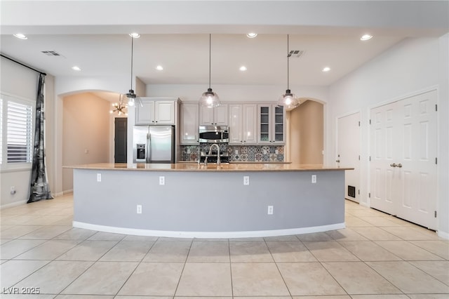 kitchen featuring stainless steel appliances, arched walkways, a large island with sink, light tile patterned floors, and recessed lighting