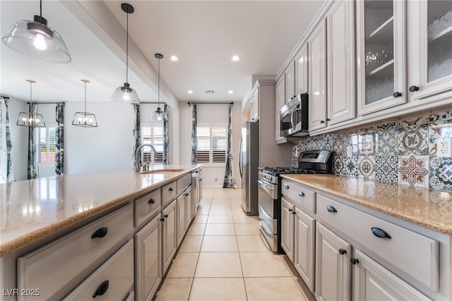 kitchen with appliances with stainless steel finishes, a sink, light tile patterned flooring, tasteful backsplash, and glass insert cabinets