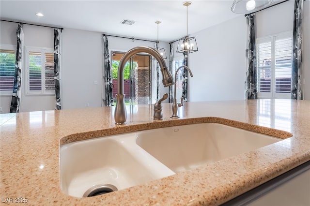 kitchen view of a sink, pendant lighting, light stone countertops, and recessed lighting