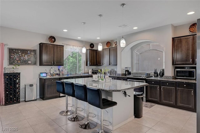 9656 Paraiso Springs St, Las Vegas, NV 89139 - kitchen with light stone counters, light tile patterned floors, dark brown cabinetry, a breakfast bar, and a center island