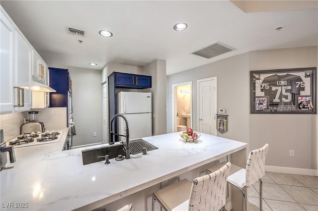 91 E Agate Ave Unit 204, Las Vegas, NV 89123 - kitchen with blue cabinetry, white appliances, a peninsula, light stone counters, and recessed lighting