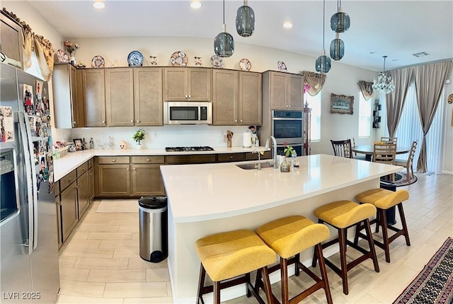 kitchen with appliances with stainless steel finishes, a sink, a breakfast bar area, light countertops, and a center island with sink