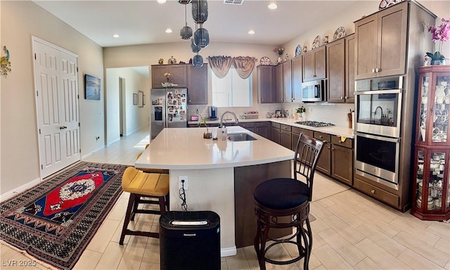 kitchen featuring appliances with stainless steel finishes, a kitchen bar, a sink, light countertops, and a kitchen island with sink