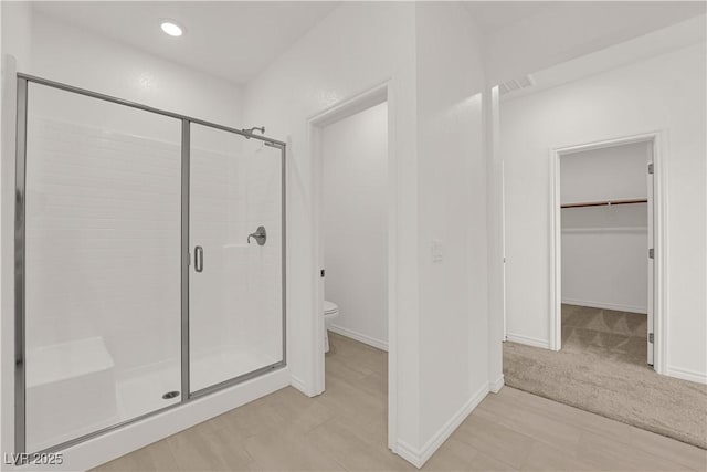 full bathroom featuring a stall shower, toilet, a spacious closet, baseboards, and recessed lighting